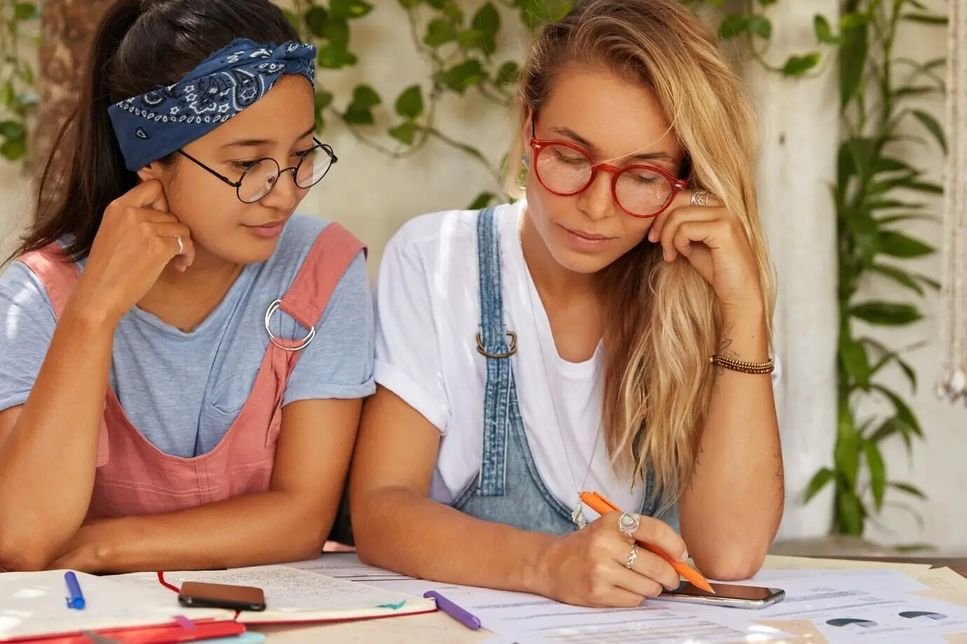 Toma horizontal de estudiantes o colegas que conversan sobre un proyecto en común; miran papeles, hacen algunas anotaciones en una libreta y sostienen un bolígrafo.